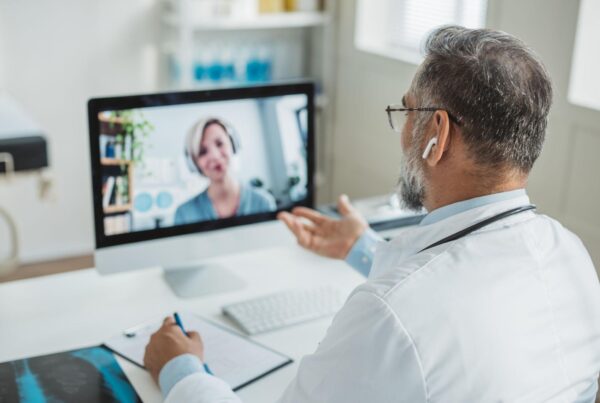 Doctor in a white coat consulting via video call with a patient on a computer screen