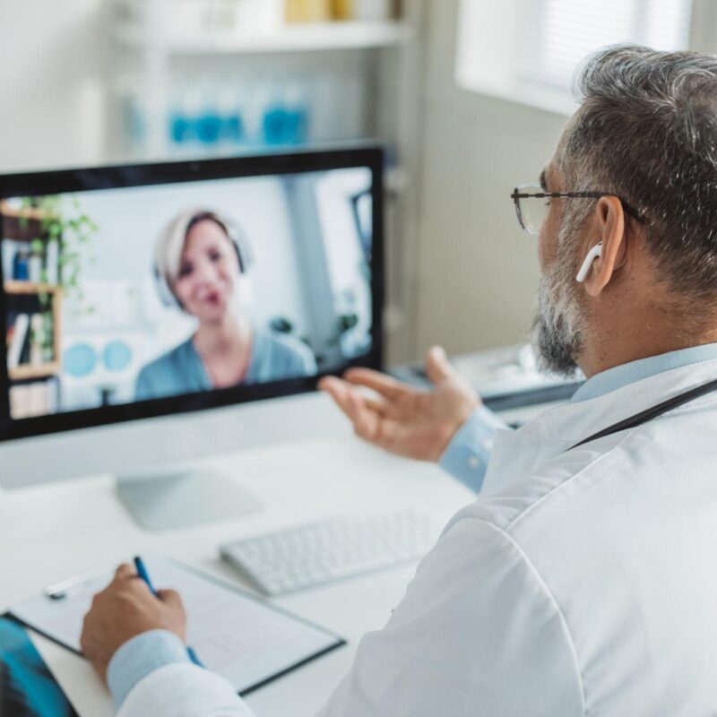 Doctor in a white coat consulting via video call with a patient on a computer screen